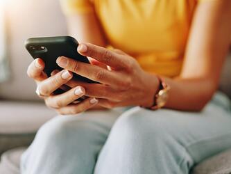 woman wearing yellow top and jeans holding and looking at phone